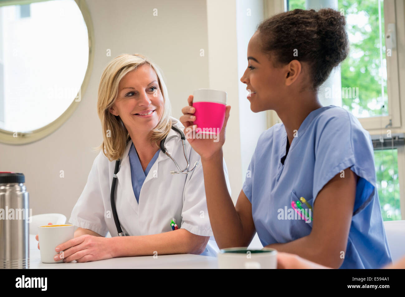 Female doctor and nurse having cup of coffee in hospital canteen Stock