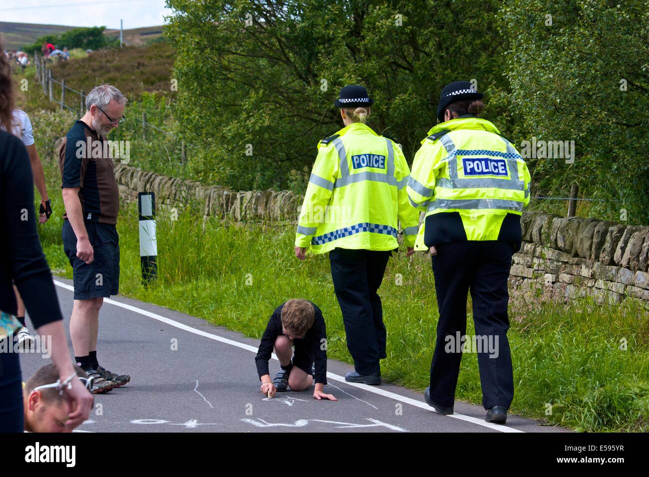 Two female police officers pass a boy writing a message with a stone on route of 2014 Tour de France through South Yorkshire Stock Photo