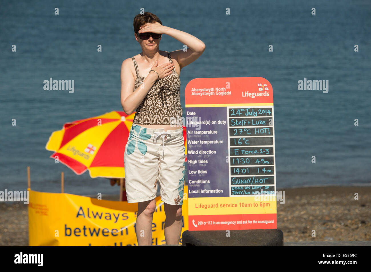Aberystwyth, Wales, UK. 24th July, 2014.  A woman looking at an RNLI lifeguard information sign, forcasting another day of hot sunny weather , with temperatures peaking at 27C at  Aberystwyth on the west Wales coast UK.  The heatwave is expected to last at least  another day, with project temperatures almost reaching 30c in some inland places, before cooler weather returns at the weekend  photo Credit:  keith morris/Alamy Live News Stock Photo