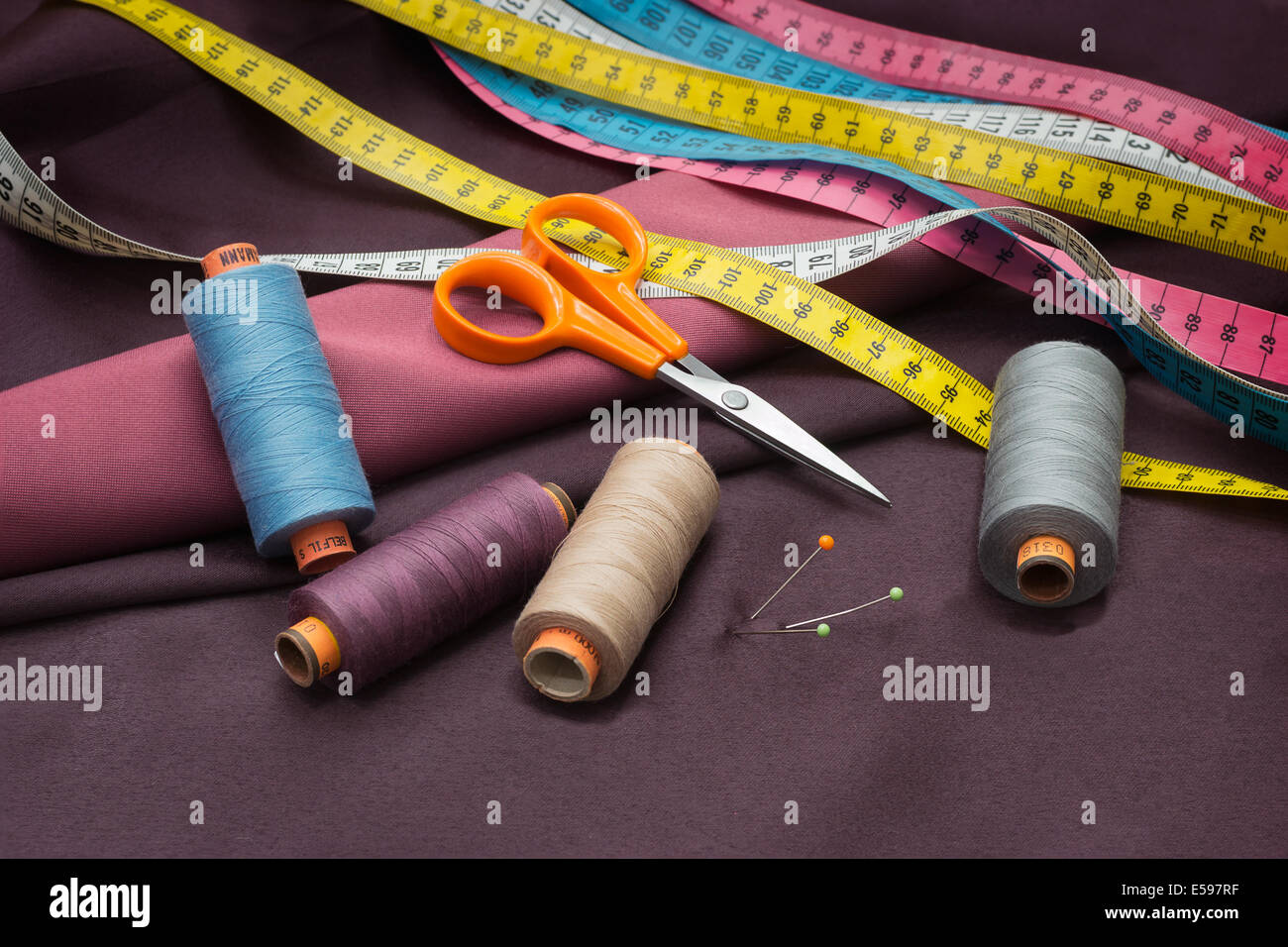 Tailors tools - thread spools, pin, scissors and measuring tape on red fabric. Stock Photo