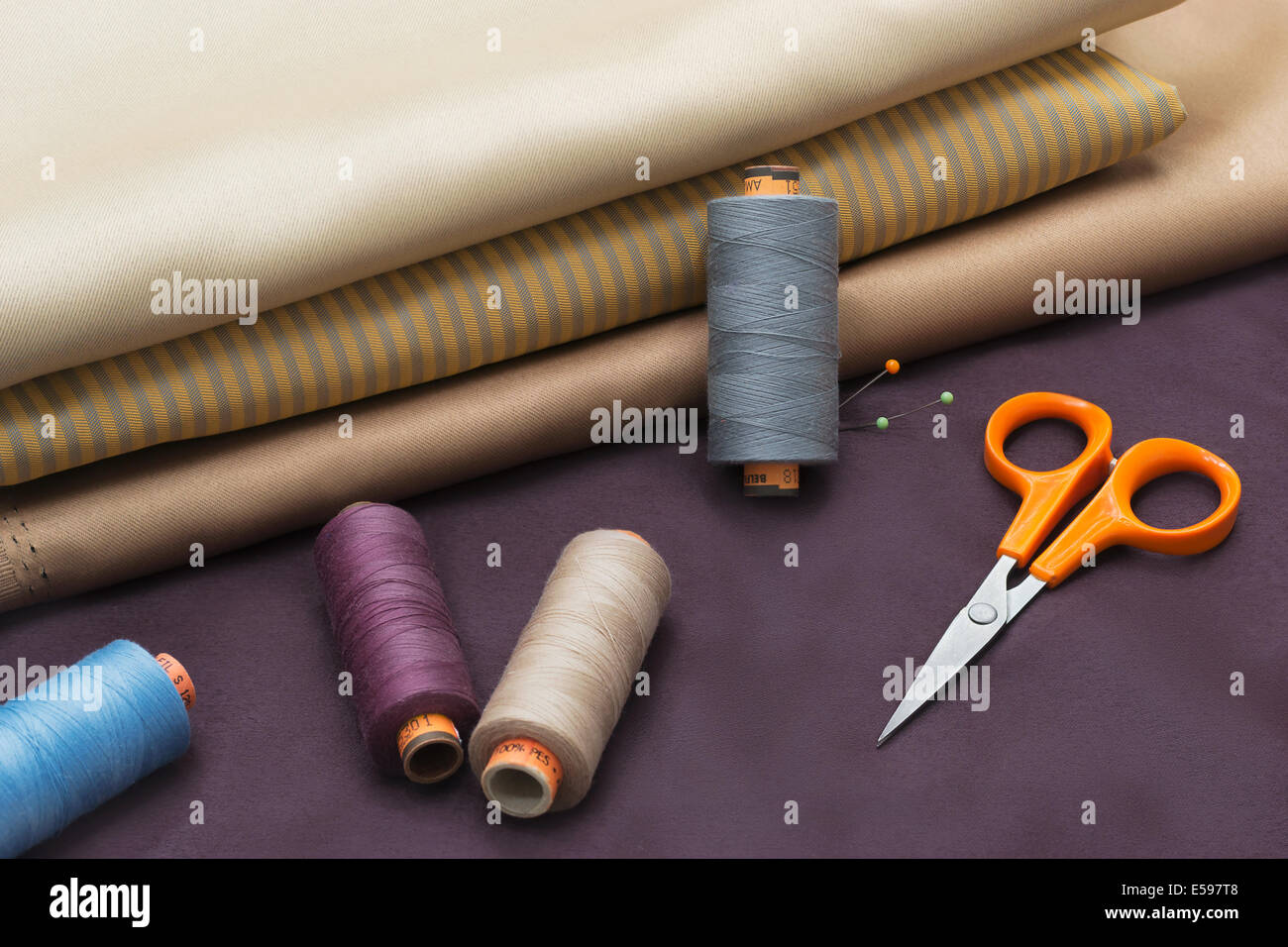 Different kind of fabric and tailors tools - thread spools, pin, scissors. Stock Photo
