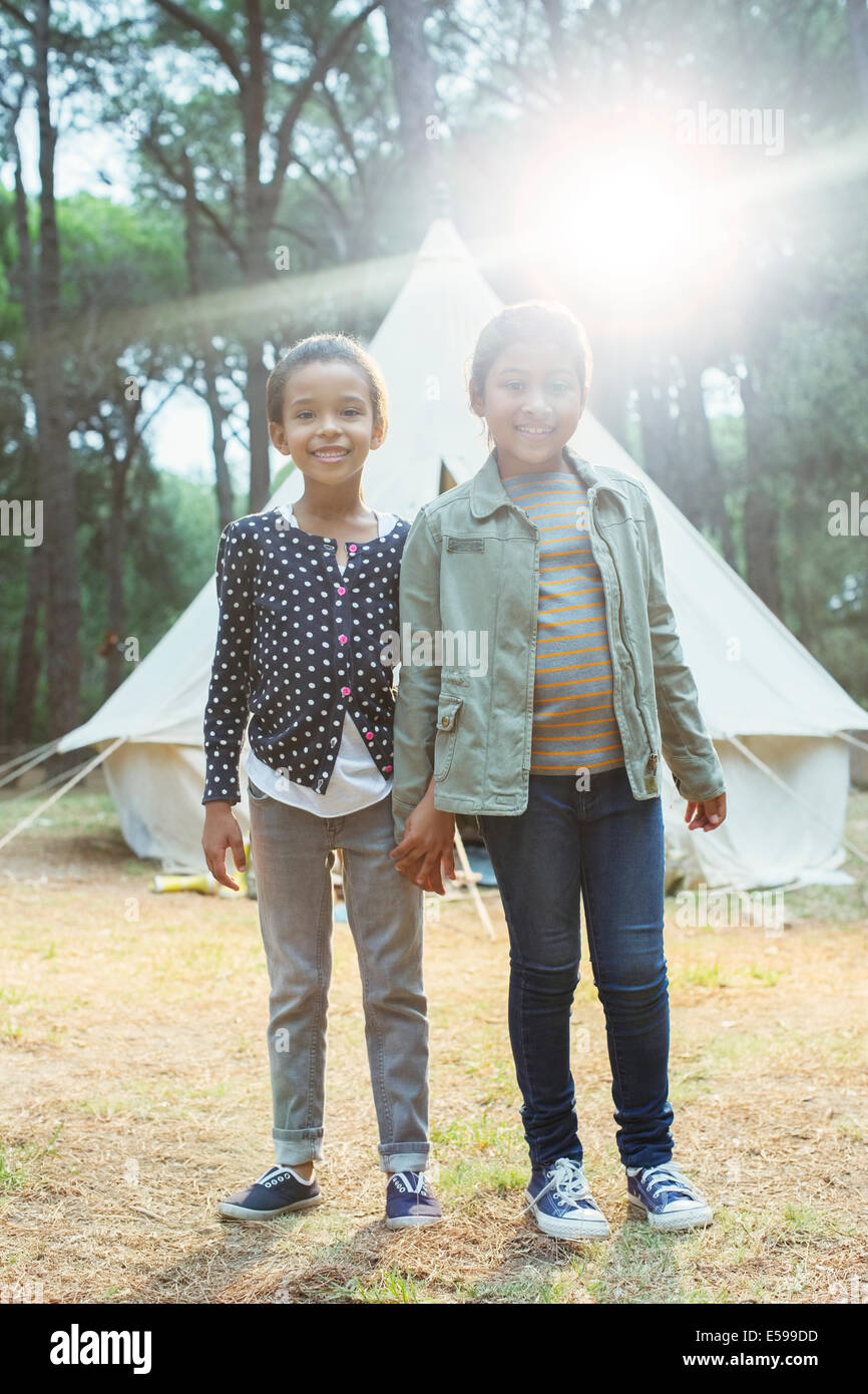 Girls smiling by teepee at campsite Stock Photo
