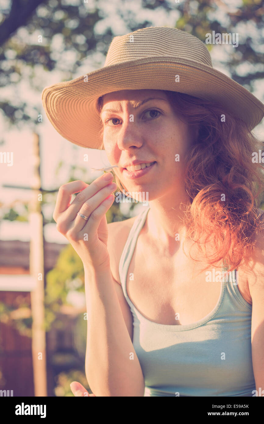 Beautiful girl with a hat smelling a flower, enjoying sunny summer day Stock Photo