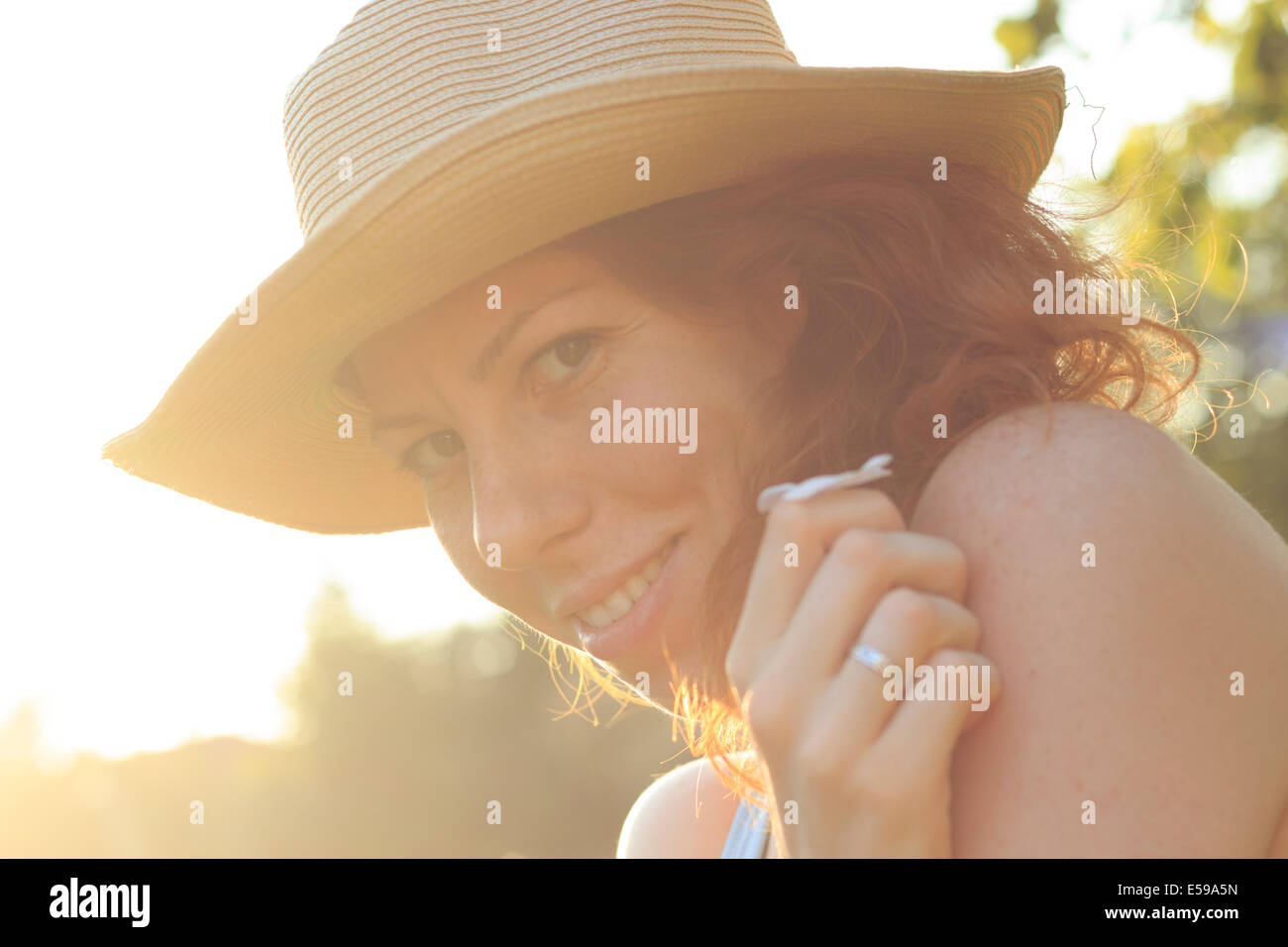 Beautiful girl with a hat smelling a flower, enjoying sunny summer day Stock Photo