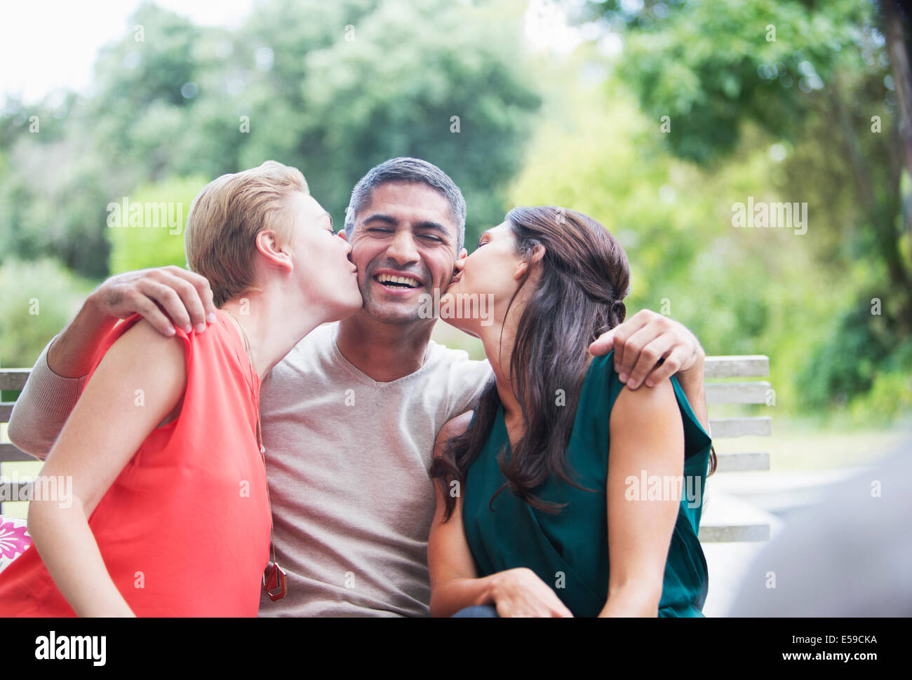 Women kissing man’s cheeks outdoors Stock Photo