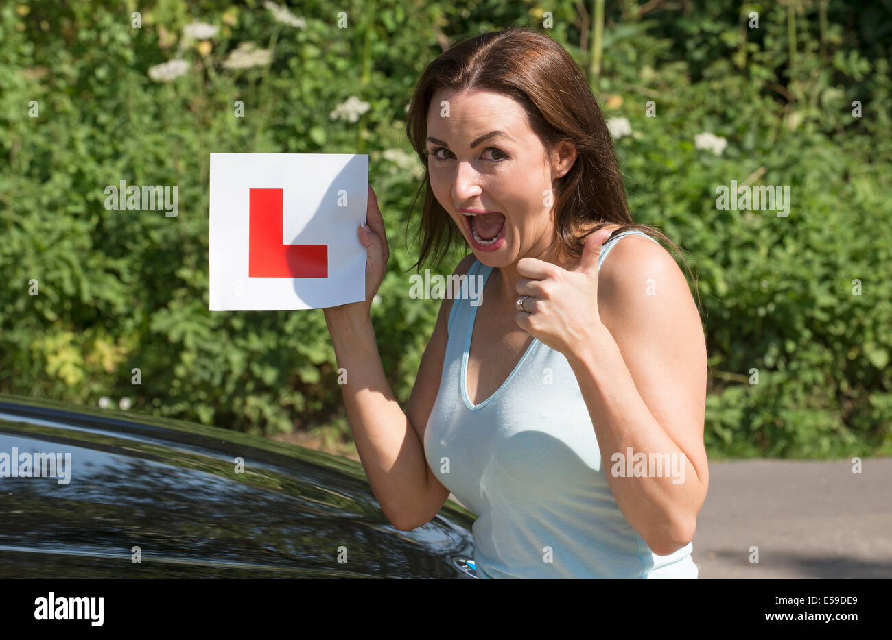 Portrait of a jubilant driver with L plate after passing her driving test. Giving a thumbs up sign Stock Photo