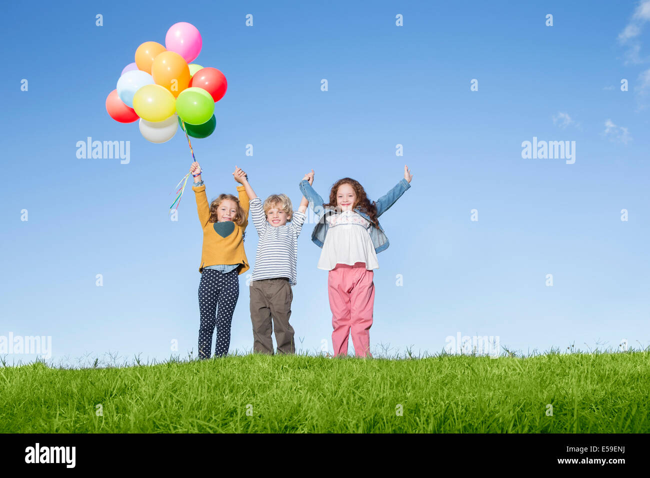 Children with balloons cheering on grassy hill Stock Photo - Alamy