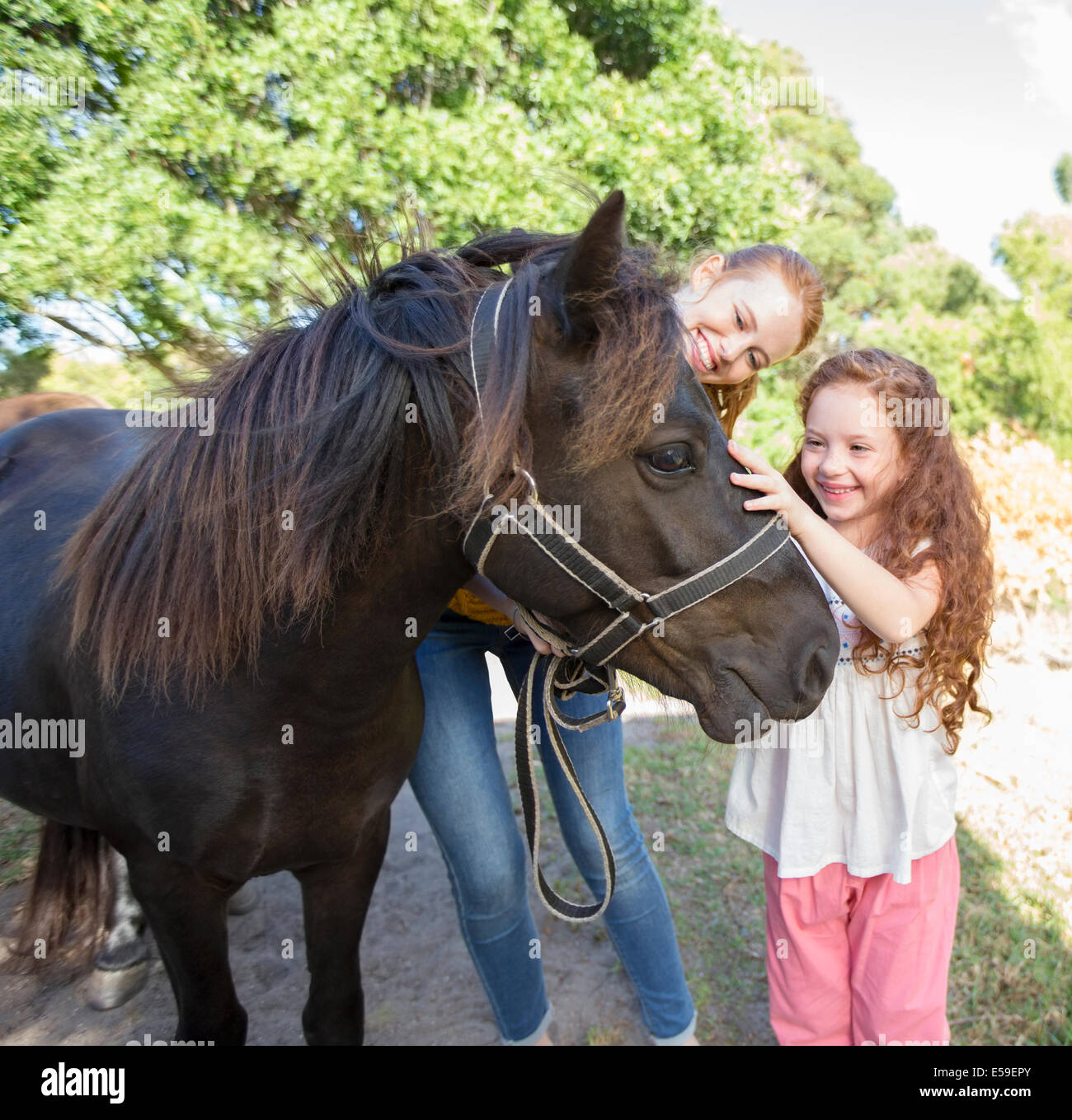 Mother and daughter petting horse outdoors Stock Photo