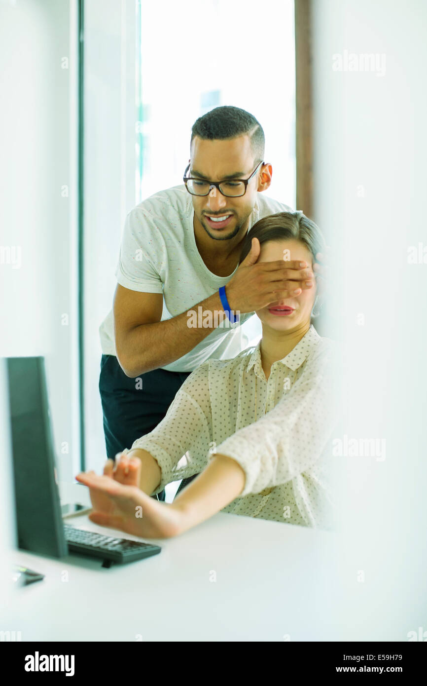 Man covering colleague’s eyes in office Stock Photo