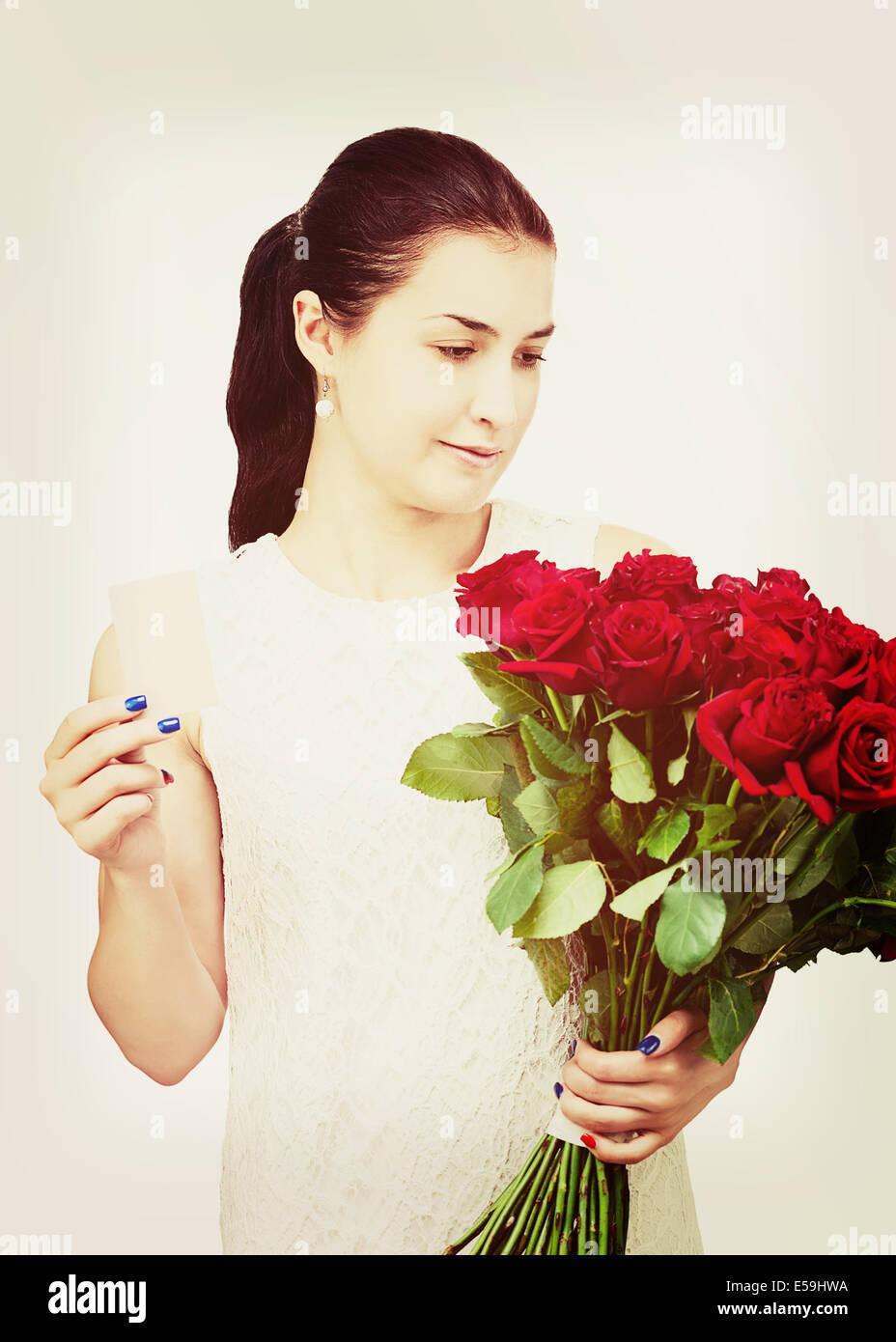 Young beautiful girl in white dress with bouquet of red roses and business card in hand isolated on white background. Stock Photo