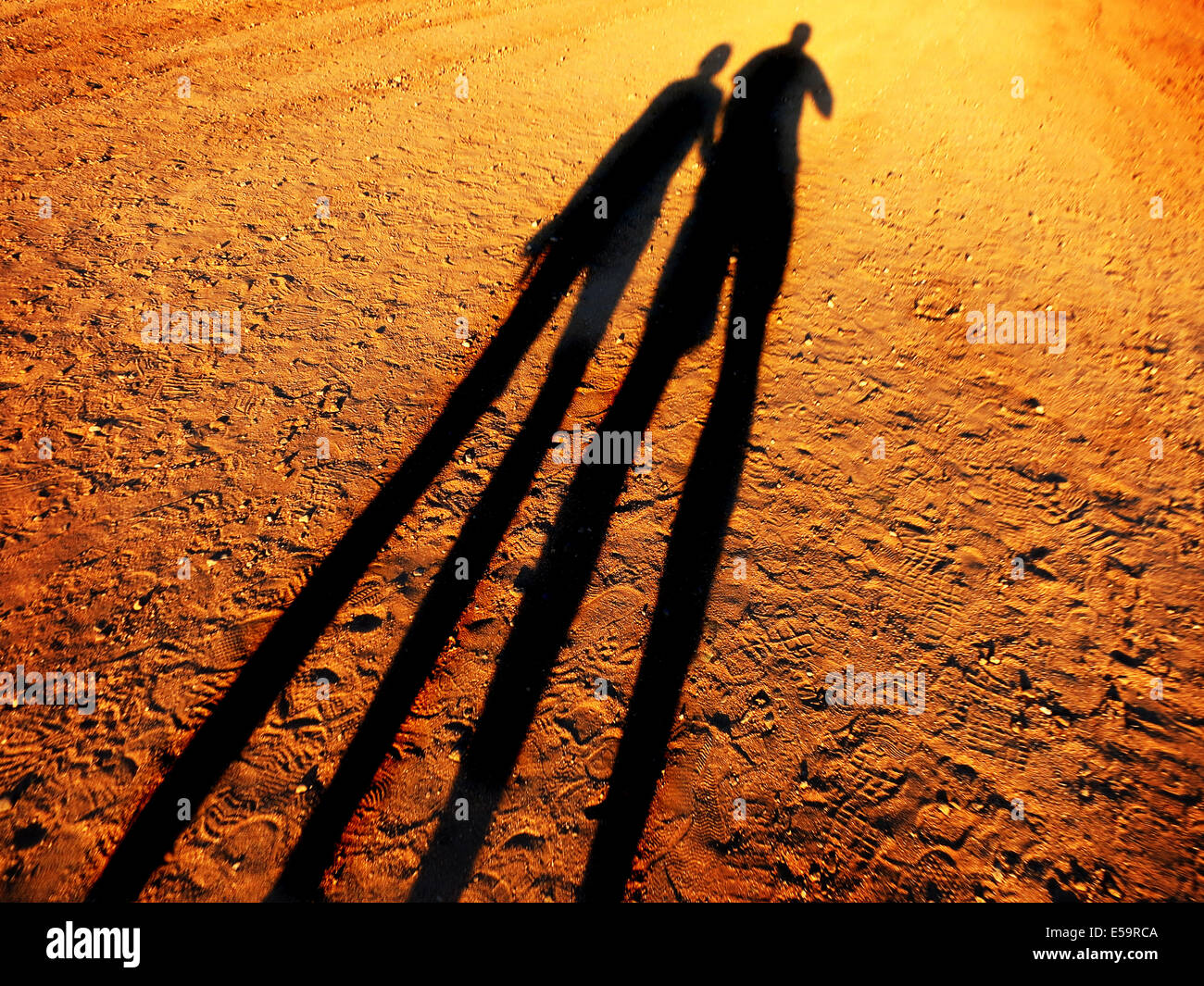 Shadow of two people holding hands walking down a dirt road together Stock Photo