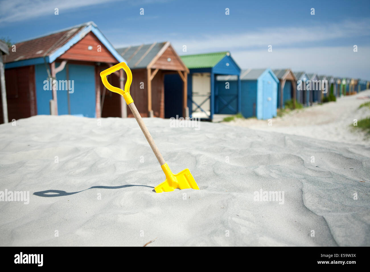 yellow childrens spade wooden painted colourful beach huts sand dunes West Wittering Sussex coast Stock Photo