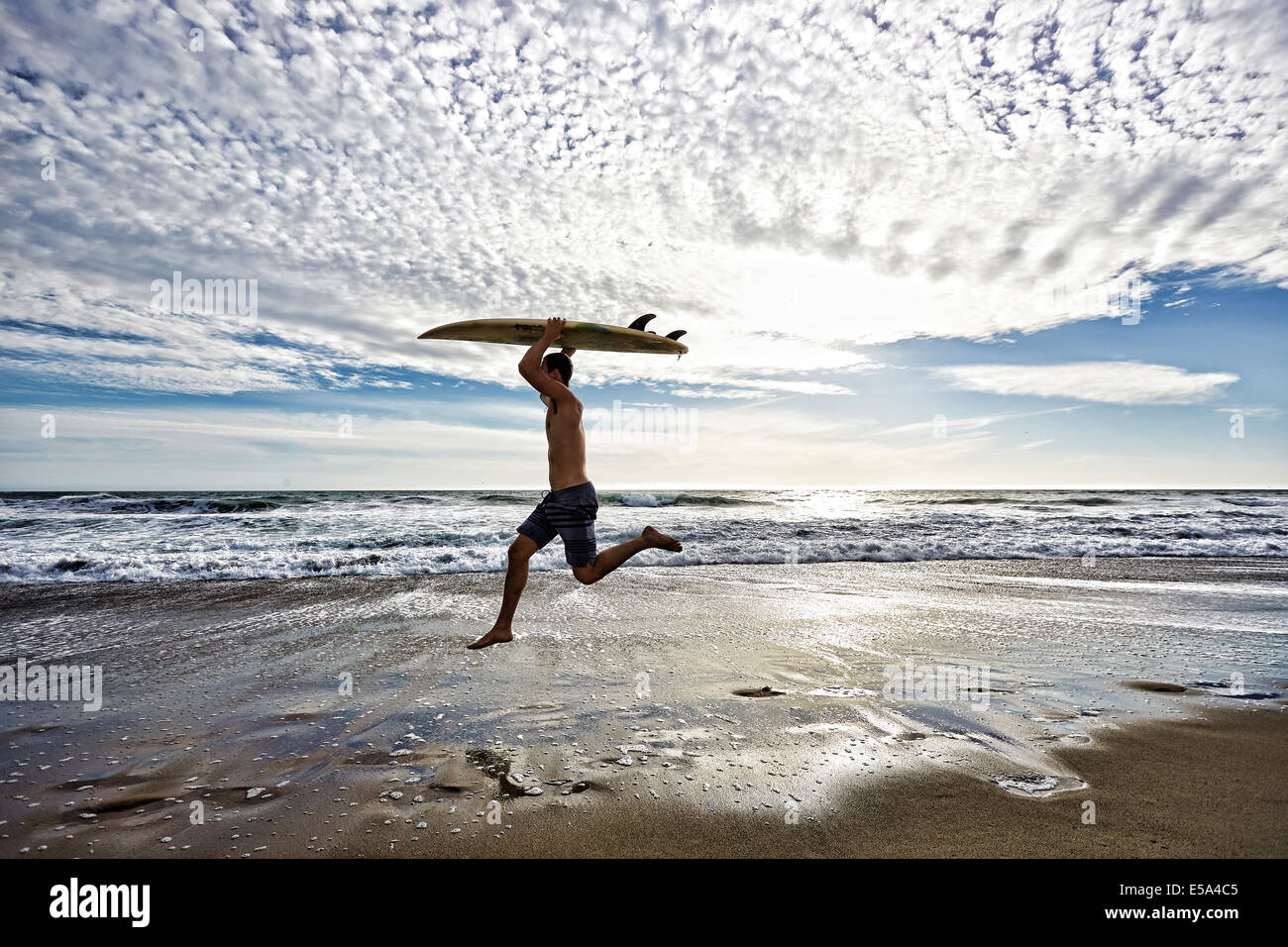 Caucasian man jumping with surfboard on beach Stock Photo