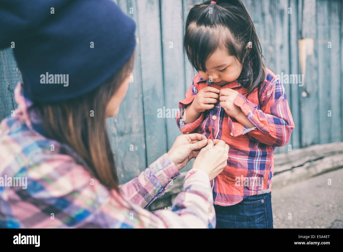 Korean mother helping daughter button her shirt Stock Photo