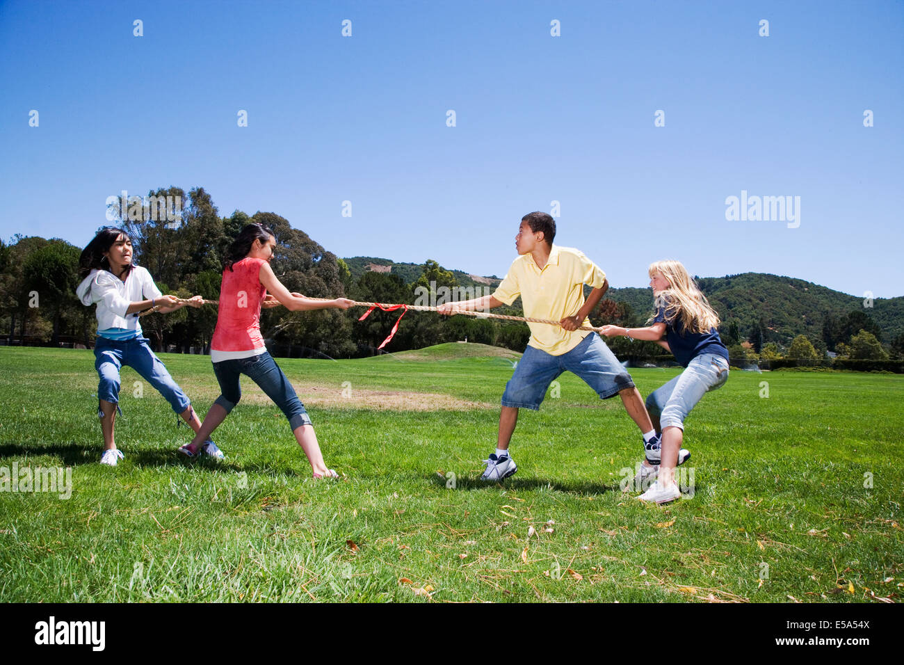 Children playing tug-of-war in field Stock Photo
