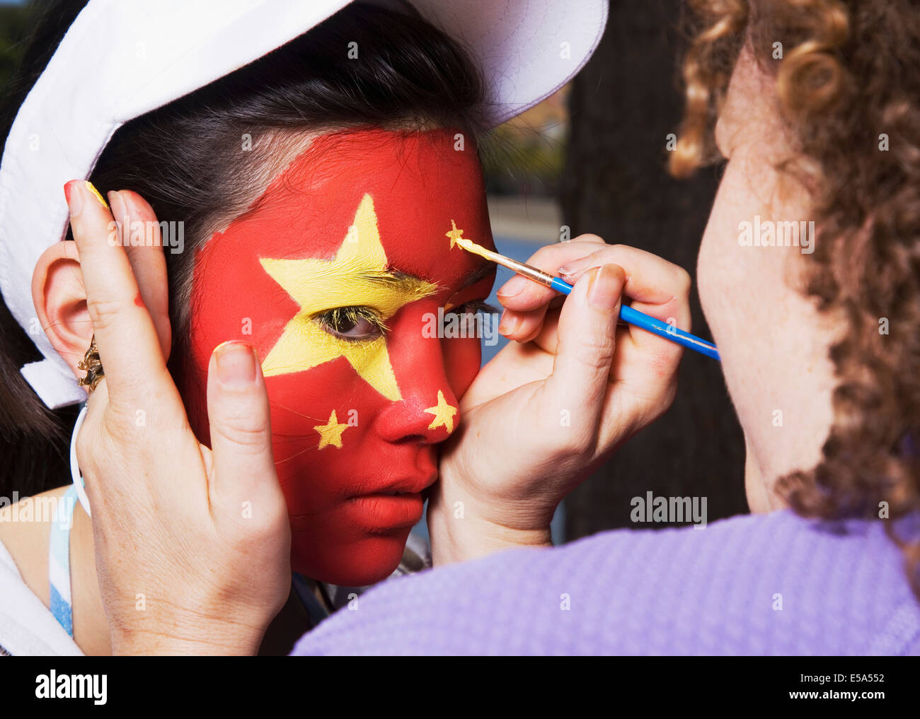 Woman painting Chinese flag on Chinese girl's face Stock Photo