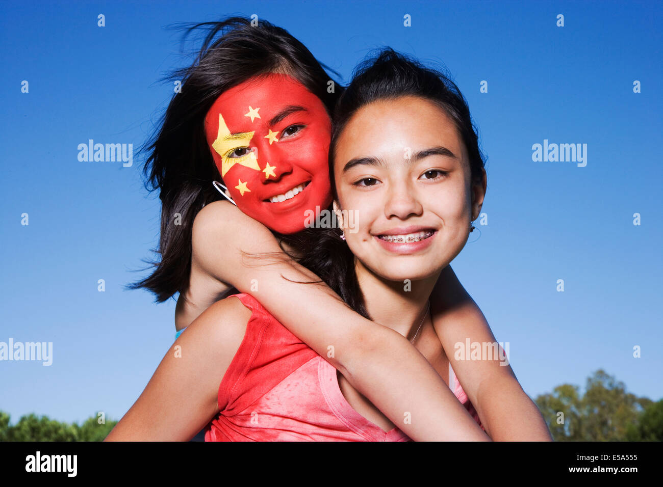 Chinese girl with Chinese flag painted on face hugging friend Stock Photo