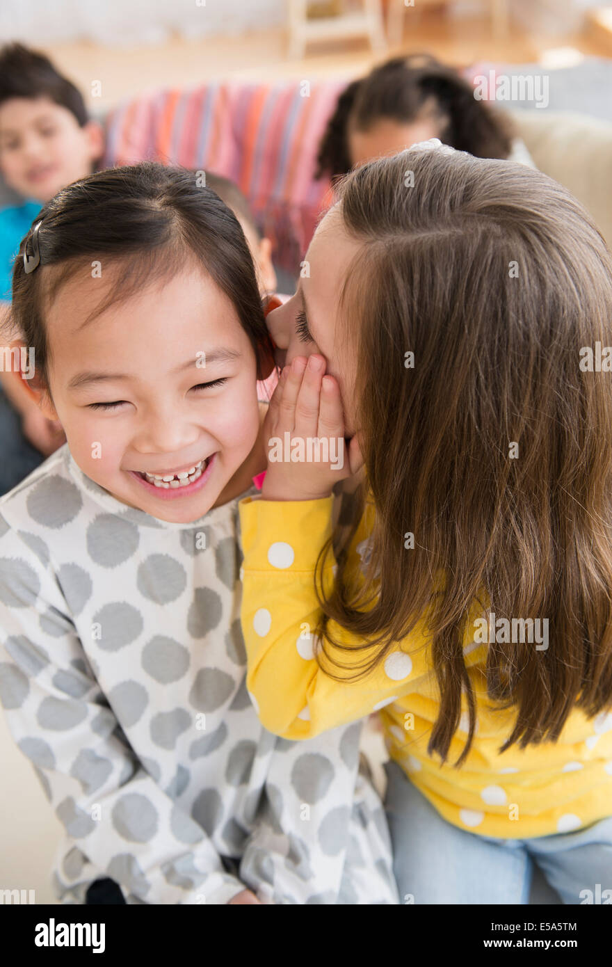 Girl whispering into friend's ear Stock Photo