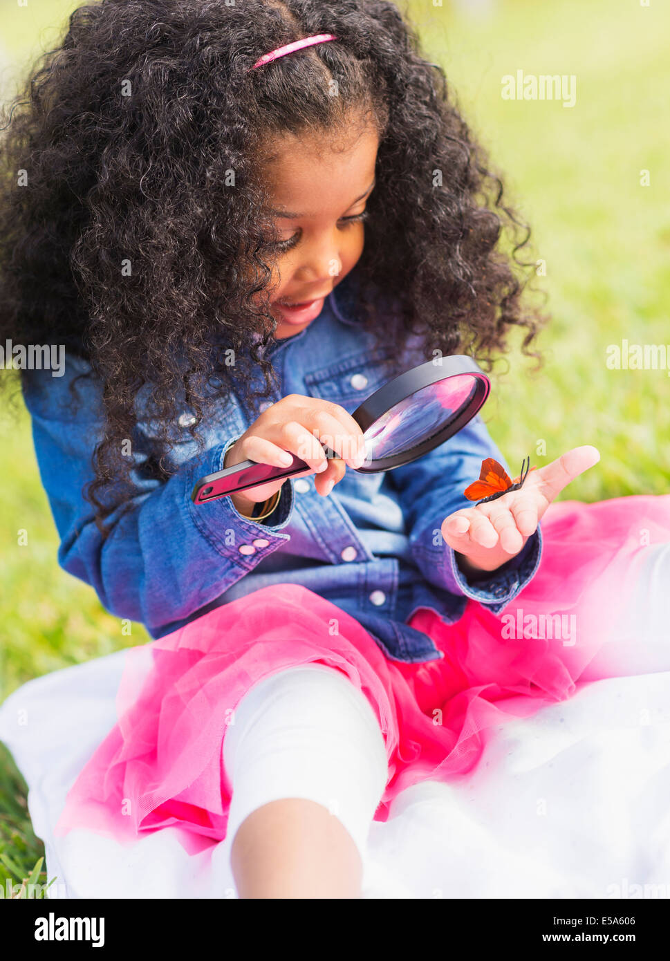 Mixed race girl examining butterfly with magnifying glass Stock Photo