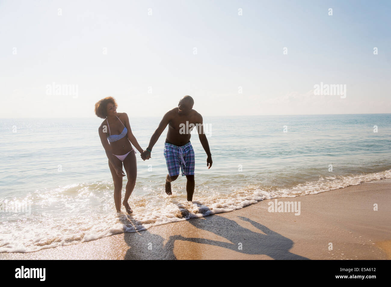 Couple holding hands in waves on beach Stock Photo