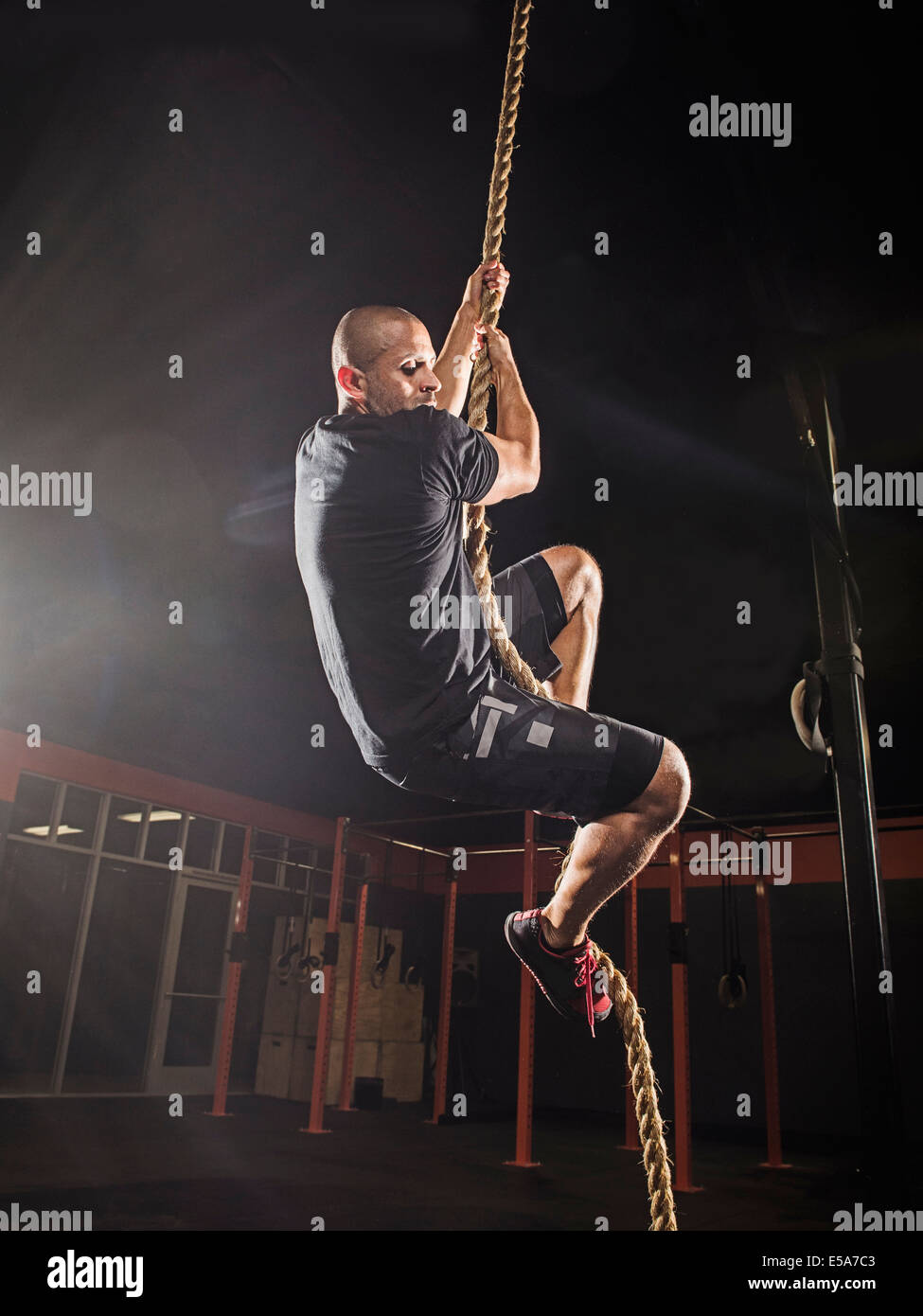 Hispanic man climbing rope in gym Stock Photo