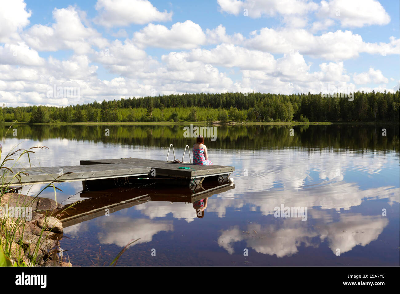 Lake scenery in summer in Finland with a woman sitting on pier Stock Photo