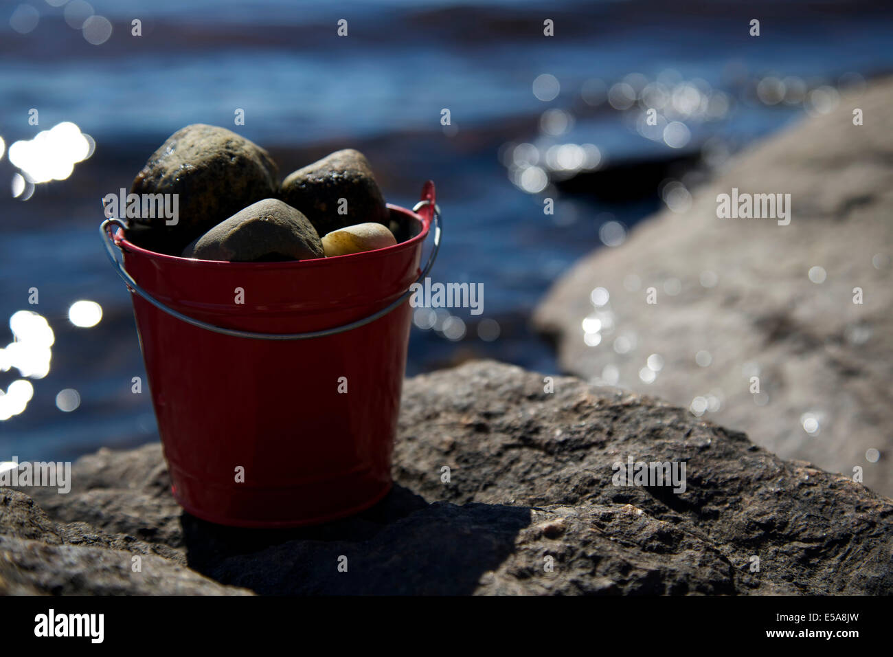 Red tin bucket full of rocks on top of a lakeside rock Stock Photo Alamy