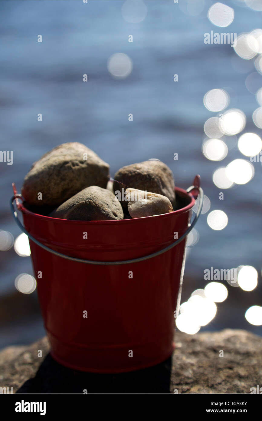 Red tin bucket full of rocks on top of a lakeside rock Stock Photo Alamy