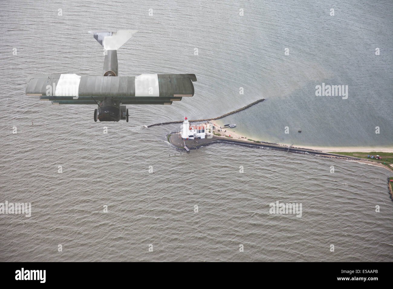 Old airplane flying above water and lighthouse Stock Photo