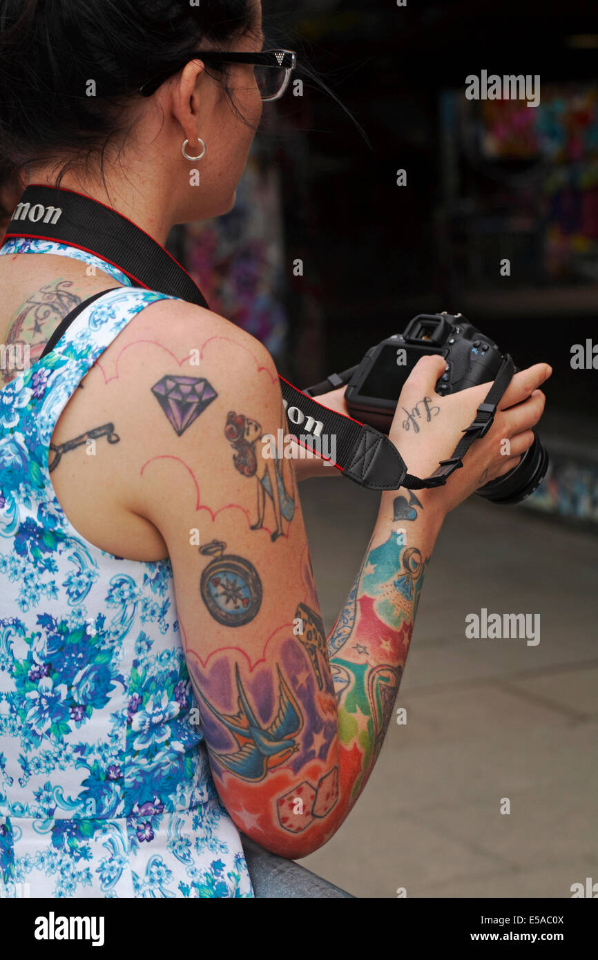 coloured tattoos covering womans arm and Life on hand holding Canon camera  Stock Photo - Alamy