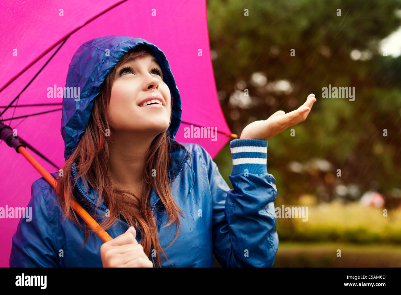 Beautiful young woman in raincoat with umbrella checking for rain, Debica, Poland Stock Photo