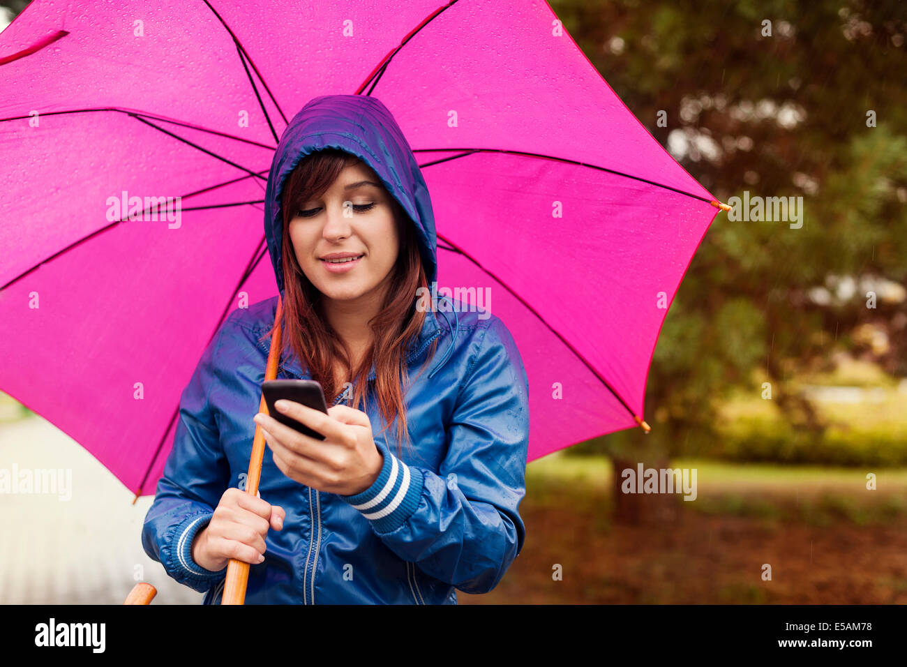 Young woman texting on mobile phone in the rain, Debica, Poland Stock Photo