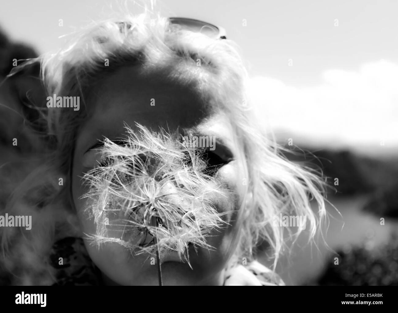 A blond woman blowing on a dandelion to make a wish BW Stock Photo