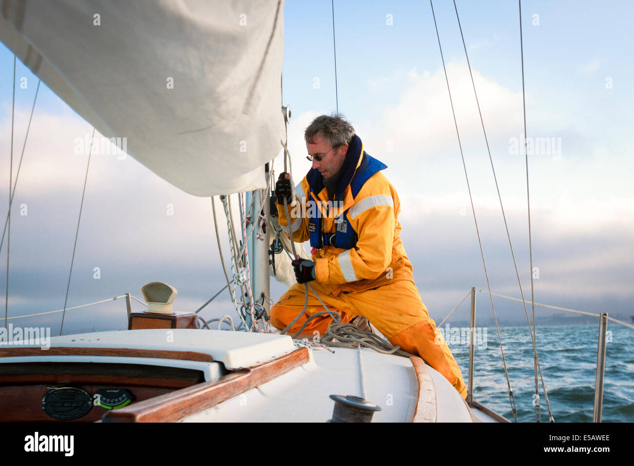 Sailor in yellow foul weather gear pulling on the halyard to raise the