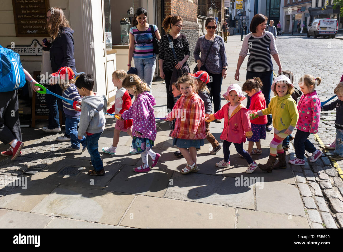 Infant school children holding hands and being led in 'crocodile' fashion along the street. Stock Photo