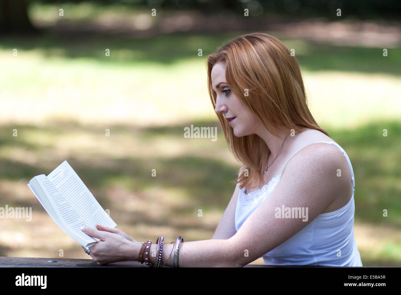 A pretty red haired young girl enjoying a book in the park Stock Photo
