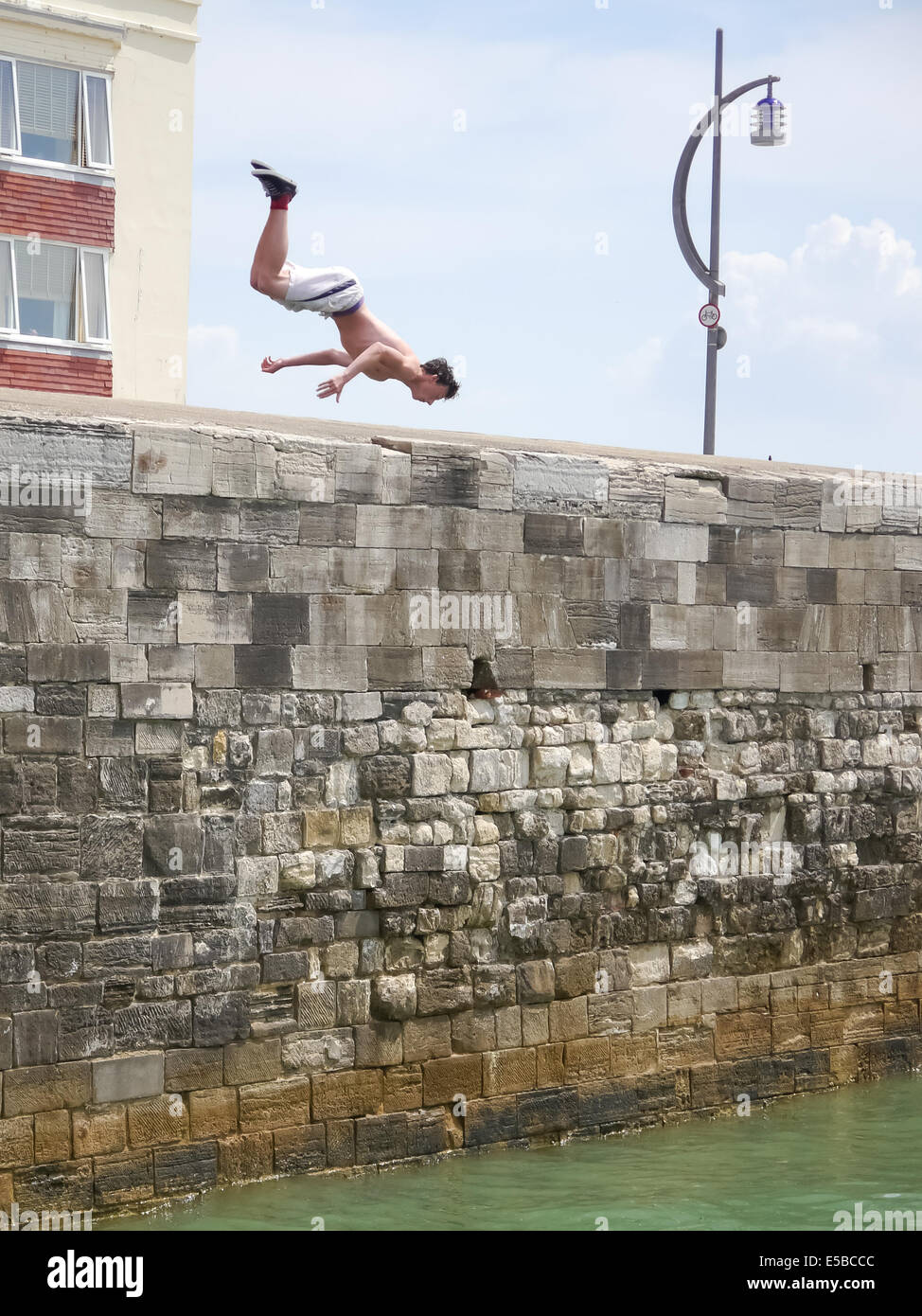 A teenage boy dives into the sea from the top of the Hot Walls in old Portsmouth. Despite serious injuries to youngsters in previous years the practice continues. Stock Photo