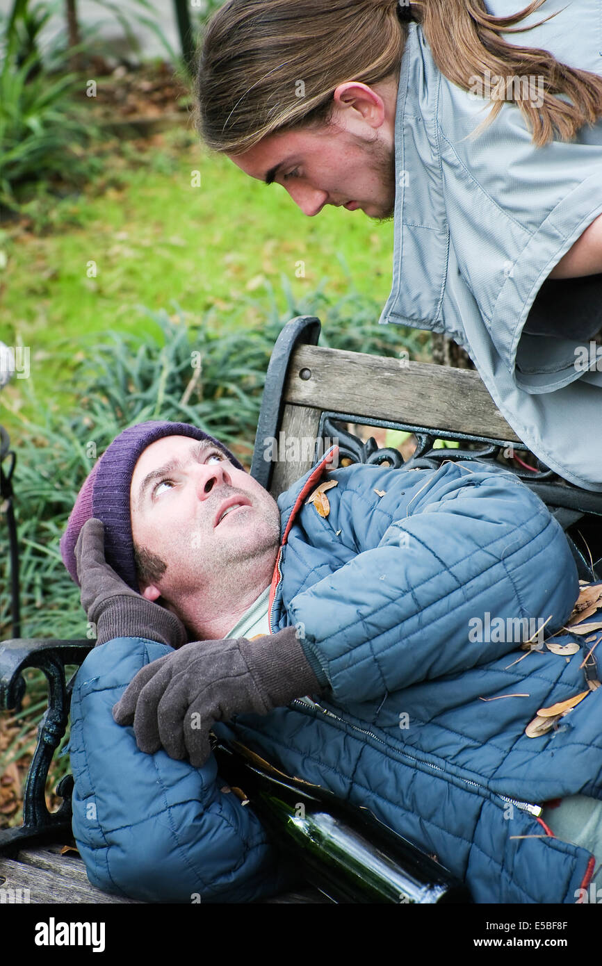 Homeless man on a park bench being threatened by an angry young man. Stock Photo