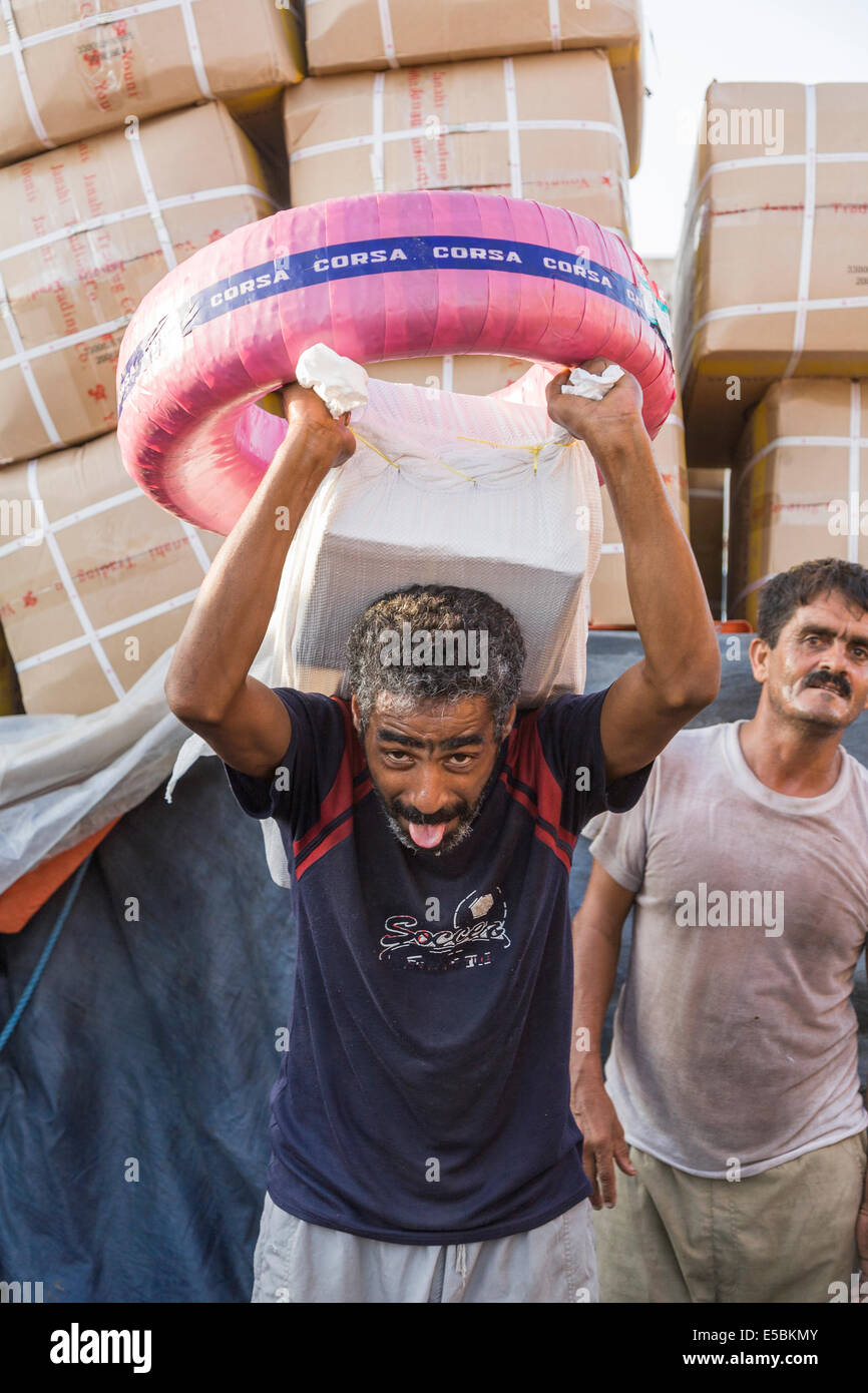 Crew member working lifting heavy box, loading cargo on to a dhow boat