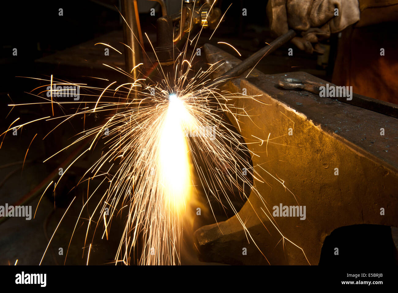 A metal fabricator utilizing a torch to heat up a piece of metal in order to shape it. Stock Photo