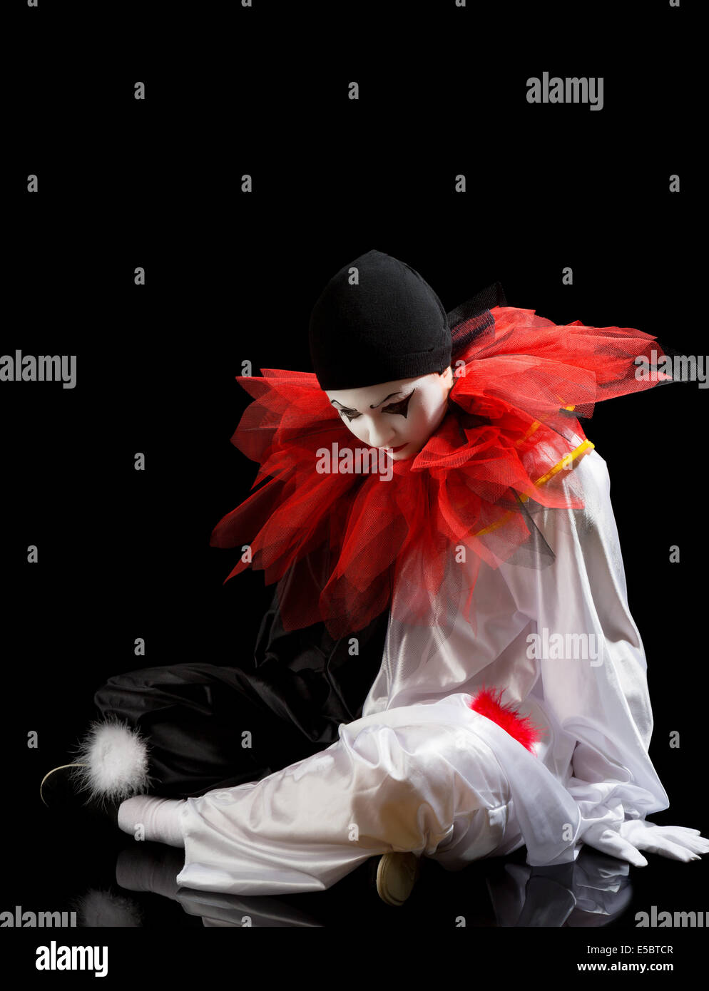 Sad Clown or Pierrot sitting on the black floor Stock Photo