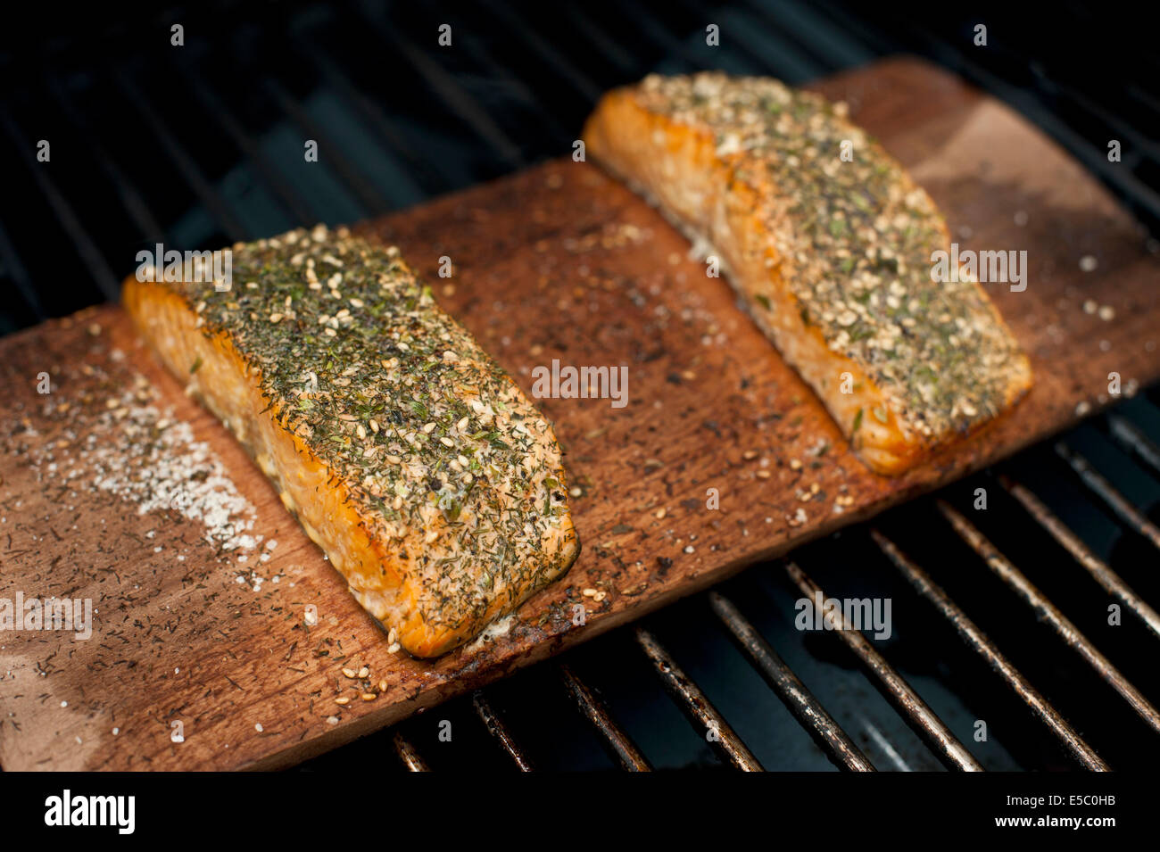 A pair of well seasoned wild Alaskan salmon fillets on a cedar plank being grilled Stock Photo