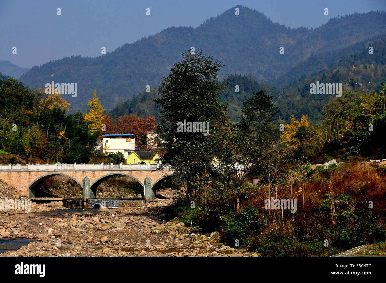 SICHUAN PROVINCE, CHINA:  A rocky river bed spanned by an arched bridge with distant mountains at Bai Lu Stock Photo