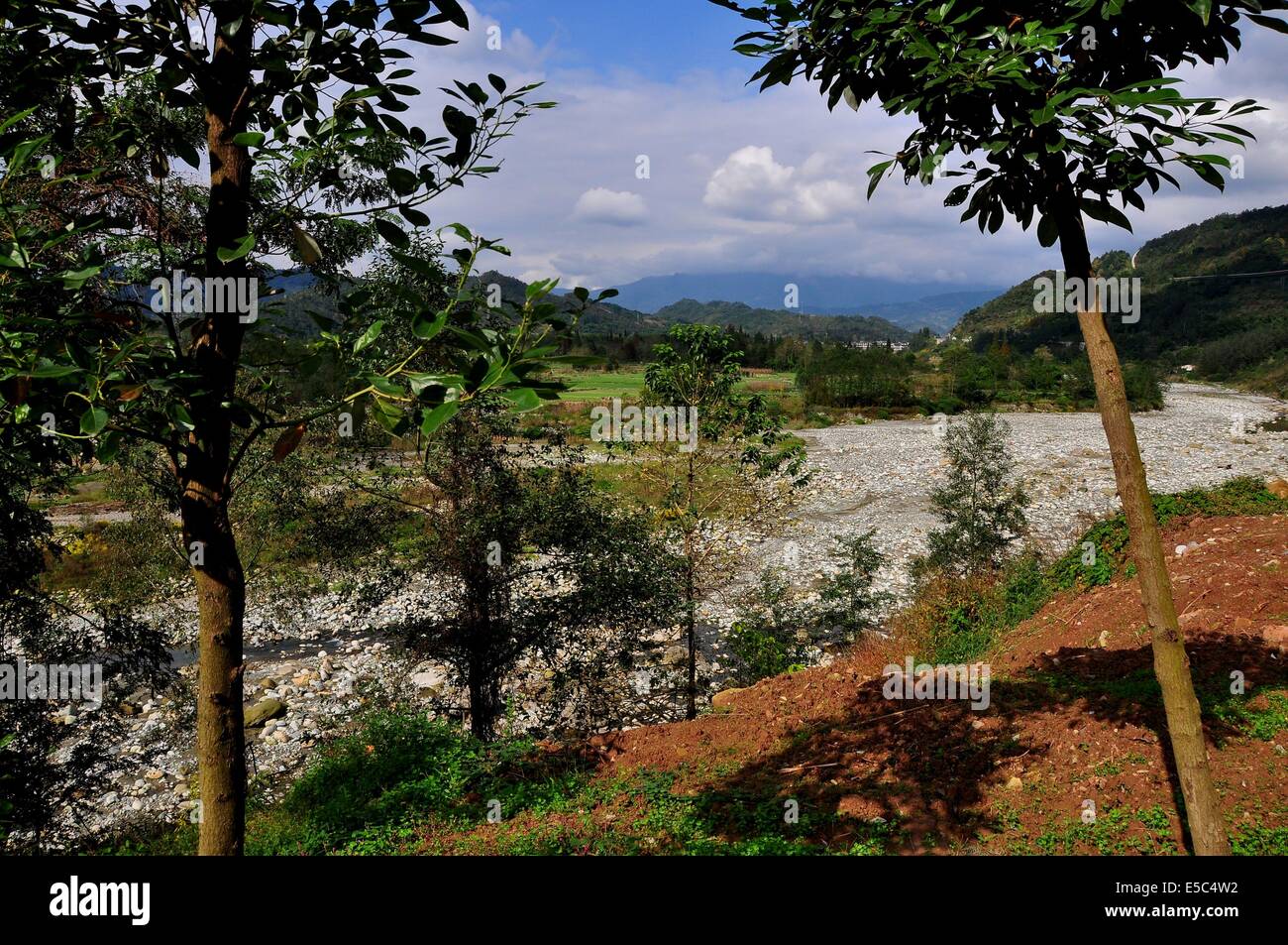 SICHUAN PROVINCE, CHINA:  View of the rock-strewn Jianjiang River, farm fields, and distant mountains Stock Photo