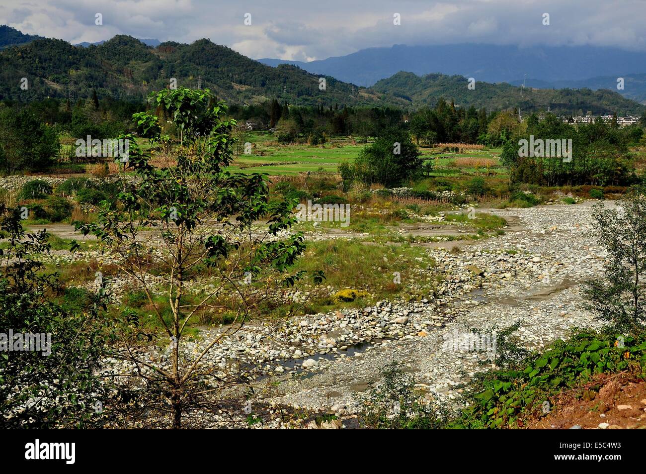 SICHUAN PROVINCE, CHINA:  View of the rock-strewn Jianjiang River, farm fields, and distant mountains Stock Photo