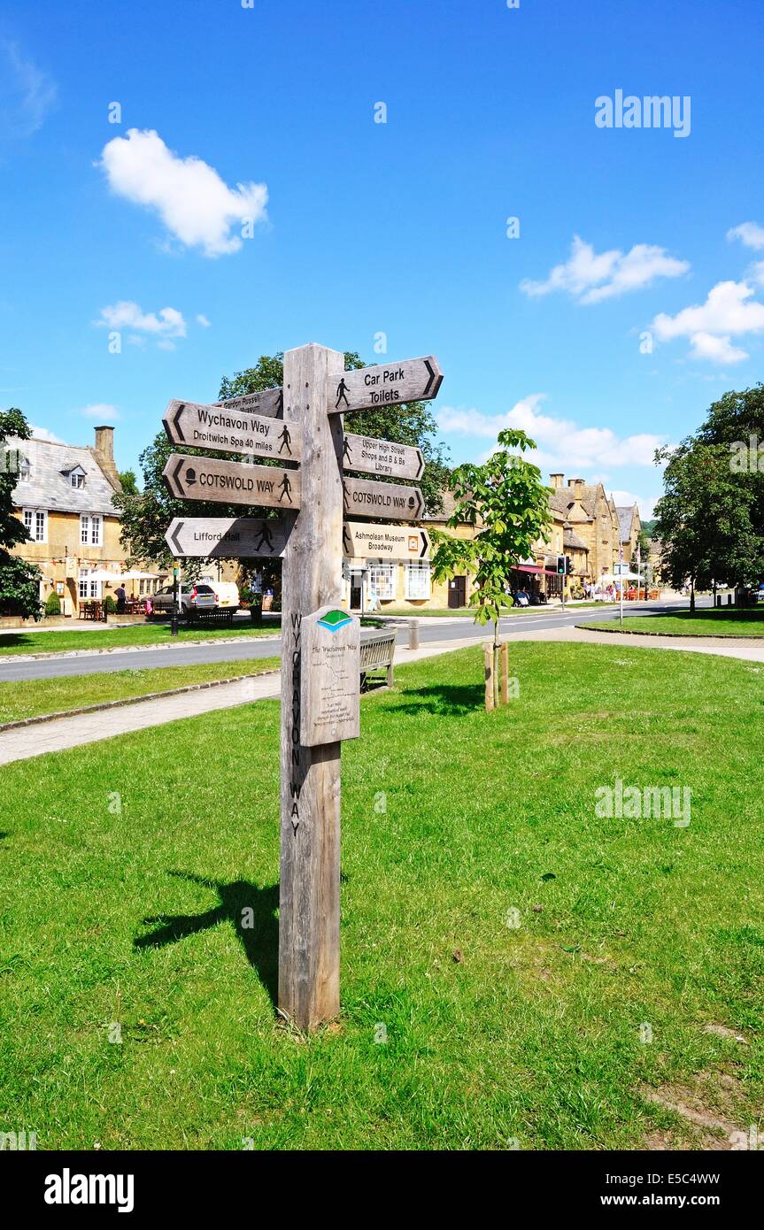 Wooden signpost on the village green along the High Street giving directions to various walks, Broadway, Cotswolds, England, UK. Stock Photo