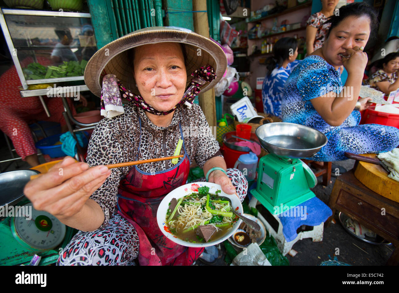 Vietnamese woman at market in 'non la' hat eating pho with chopsticks Stock Photo