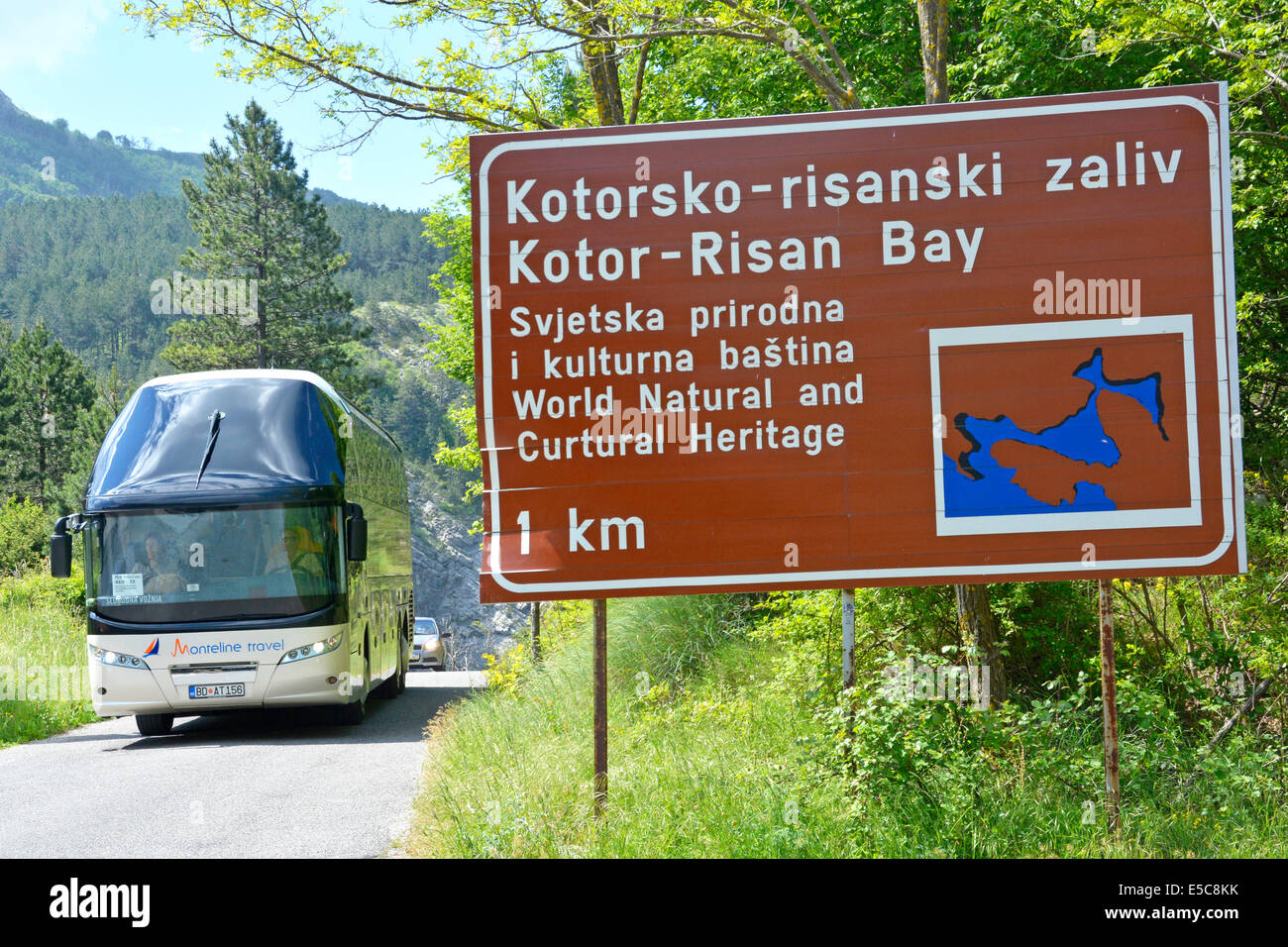 Coach tour driving along narrow mountain road passing brown tourist information roadside sign within Lovćen National Park Stock Photo