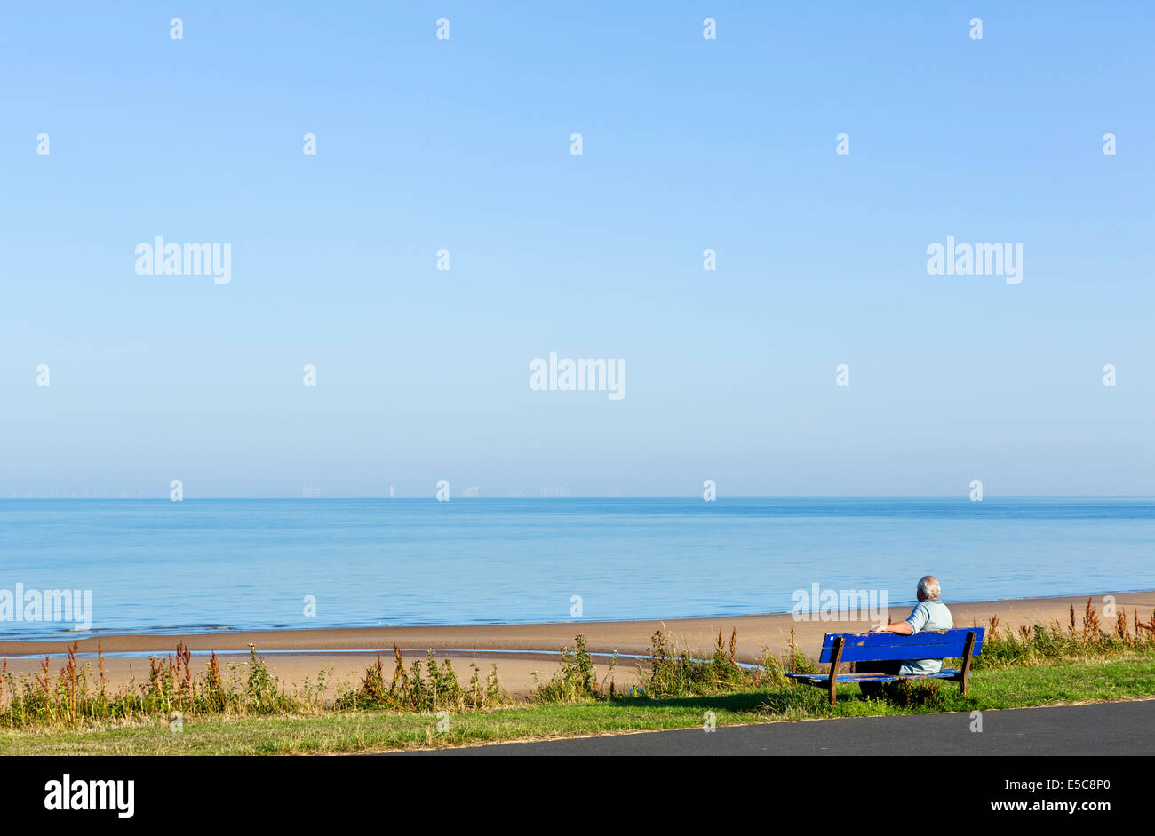 Man sitting on a bench on the seafront at Thornton Cleveleys in the early morning, North Blackpool, Lancashire, UK Stock Photo