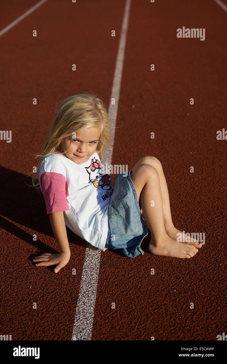 Child little blond girl sitting on tartan Running track at stadium